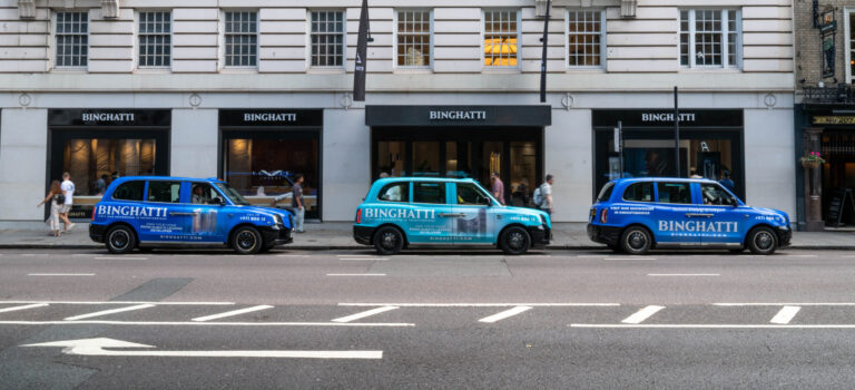 London taxi advertising with branded cab wraps - Excite Out Of Home “Branded London taxis with Binghatti advertising wraps parked on a London street, showing taxi advertising in action.