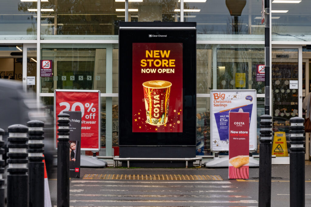 Digital retail media screen outside a supermarket promoting a new store opening, reaching shoppers at the point of purchase