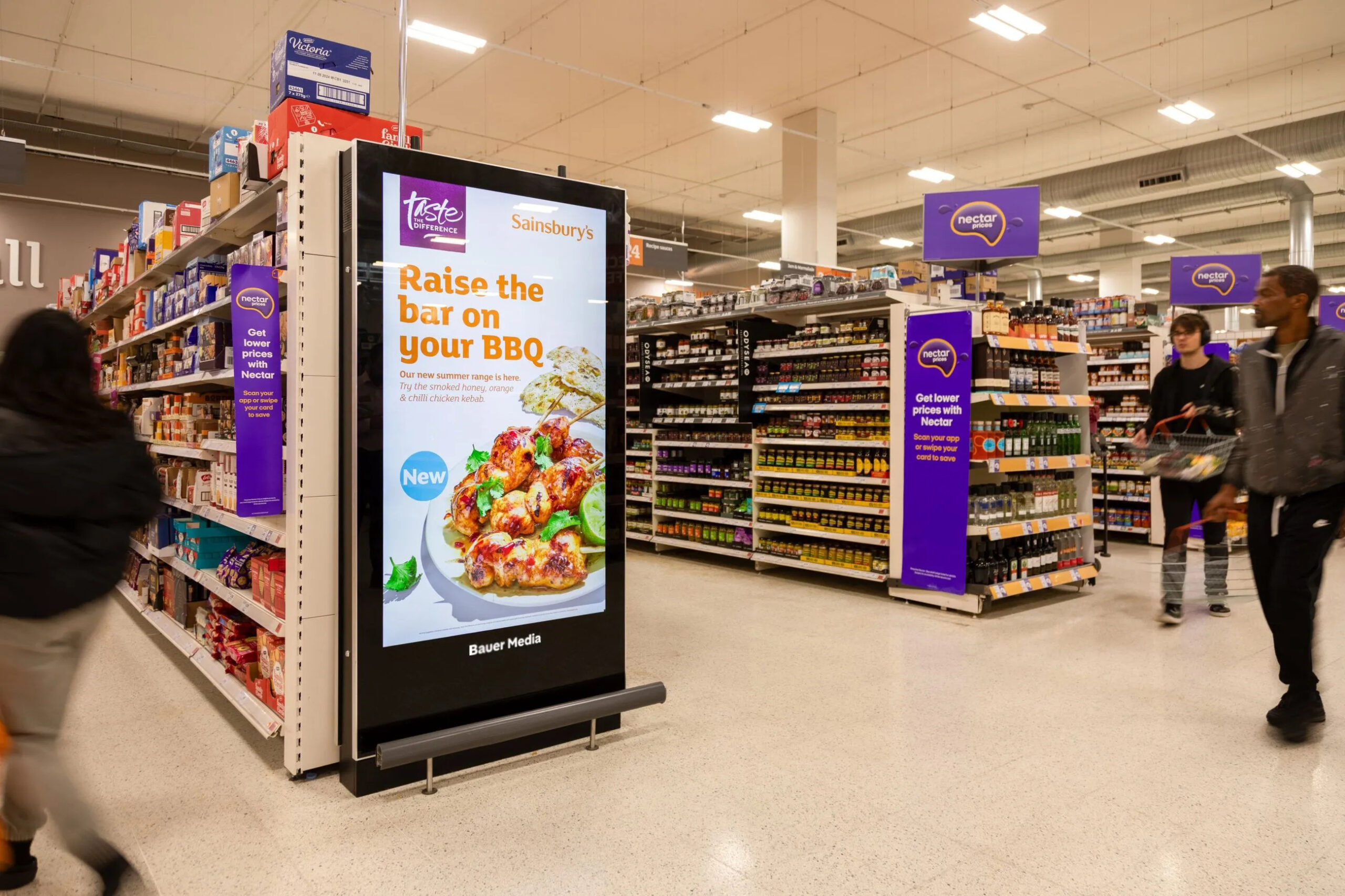 In-store digital advertising screen placed within a supermarket aisle reaching shoppers while browsing products