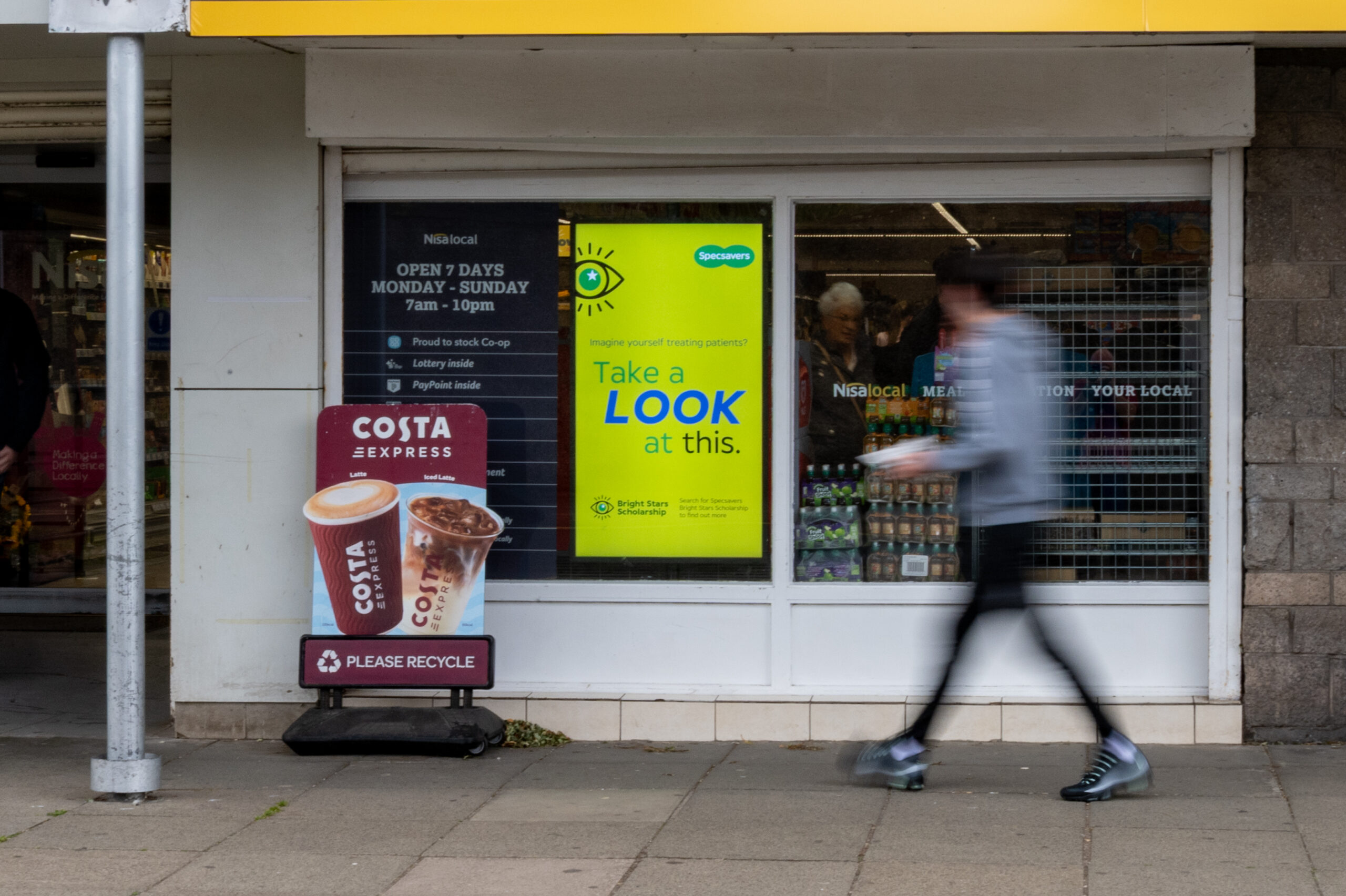 Digital advertising screen outside a convenience store influencing shoppers at the point of entry